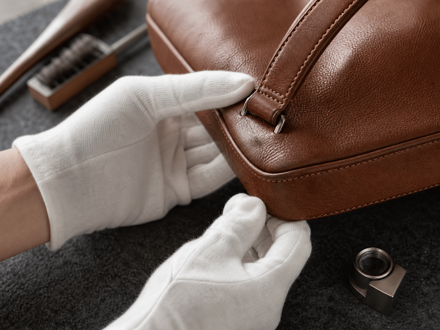 Gloved hands reviewing the stitching and leather condition of an unbranded pre-owned bag